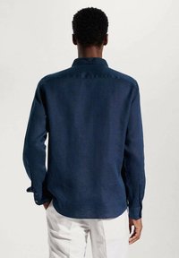 Chemise à manches longues bleu marine, en mélange de lin, avec un col standard, des poignets boutonnés et un ourlet droit, présentant une texture lisse.