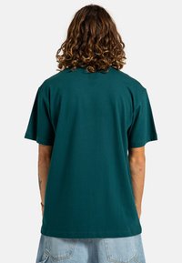Camiseta de algodón color teal con mangas cortas, cuello redondo y corte relajado. Textura suave sin patrones o acentos visibles.