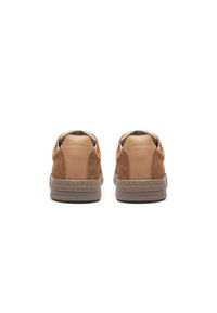 Brown suede sneakers with tan leather accents, rounded shape, and a textured rubber sole. Features stitching detail along the edges.