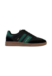 Chaussure de sport avec une tige en tissu noir, des accents à rayures vertes et une semelle en caoutchouc marron. Présente "TEDDY SMITH" et "1989" en lettres dorées.