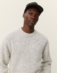 Pull en maille gris clair à motifs avec un col rond. Porté avec une casquette noire à motifs, présentant un bord légèrement incurvé et un tissu texturé.