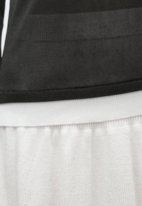 Must teksaga ülaosa ribikangast ja valge tekstuuriga alaosa, millel on elastne vöökoht, rõhutades kontrastseid värve ja materjale.