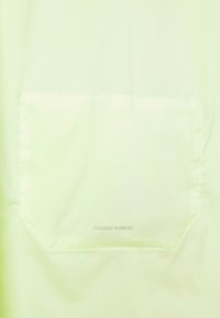 Tela verde claro con un bolsillo cuadrado cosido etiquetado "PRenda PLEGABLE" en un texto gris tenue.