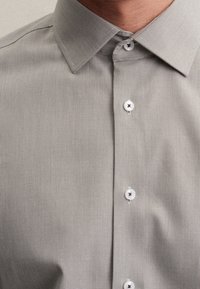 Ljusgrå skjorta med knappar och en subtil rutmönster, spetskrage och vita knappar, med slätt tyg och rena linjer.