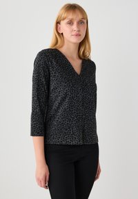 Haut noir à col en V avec manches trois-quarts, présentant un motif léopard texturé. Confectionné dans un tissu doux avec une coupe décontractée.