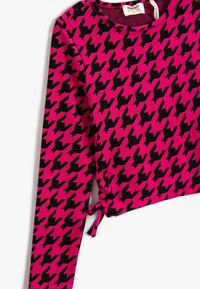 Camiseta de manga larga rosa con un patrón de espiga negro. Presenta un detalle fruncido en el dobladillo. Fabricada con una tela suave y elástica.