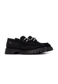Scarpe slip-on in suede nero con una suola in gomma spessa, dotate di due accenti metallici sul davanti e dettagli testurizzati sulla suola.