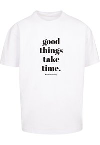 Hvid bomulds T-shirt med sort tekst, der står "gode ting tager tid." under en hashtag. Klassisk crew neck og korte ærmer.