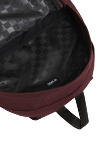 Mochila marrón con un patrón interior de tablero de ajedrez negro. El interior cuenta con un forro de tela suave y una pequeña etiqueta de marca.