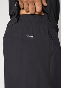 Sorte ClimaCool-shorts med elastisk linning, der har en lynlåslomme i siden, glat tekstur og let design.