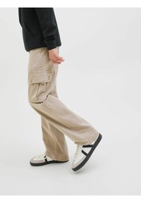 Beiga cargobyxor med flera fickor, avslappnad passform, tillverkade av bomull och med subtilt mönster, kombinerade med svarta och vita sneakers.