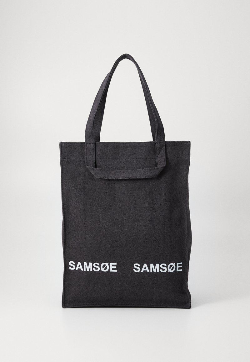 Black canvas tote bag with two top handles, featuring white "SAMSØE" text printed on the front. Simple, rectangular design.