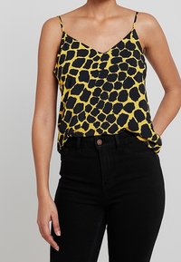 Top giallo con stampa leopardata nera, dotato di spalline regolabili e scollatura a V, abbinato a jeans neri a vita alta.