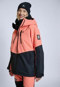 Rosa og sort isoleret jakke med hætte, der har et logo-patch på ærmet og lynlås-lommer. Blødt tekstureret stof.