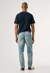 Marineblaues Baumwoll-T-Shirt mit kurzen Ärmeln, kombiniert mit hellblauen Jeans. Die Jeans haben eine ausgewaschene Optik und klassische Gesäßtaschen.
