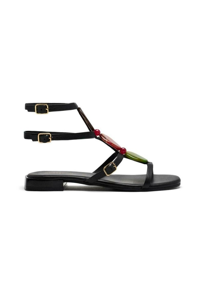 Sandalias planas negras con múltiples correas en el tobillo, que cuentan con elementos decorativos coloridos en rojo, verde y marrón. Las hebillas doradas acentúan el diseño.