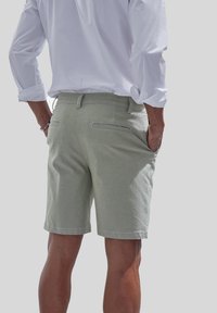 Helle grüne Shorts aus weichem Stoff, mit hinteren Taschen und kontrastierenden Nähten. Kombiniert mit einem weißen Langarmshirt.