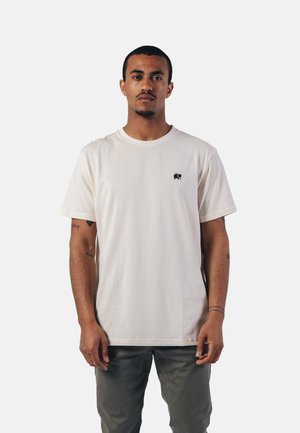 Camiseta de algodón color marfil con cuello redondo y mangas cortas, que presenta un pequeño logotipo de elefante negro en la parte izquierda del pecho.