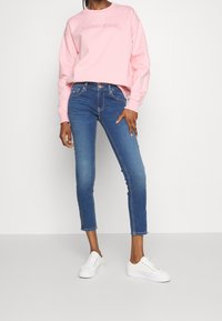 Sudadera rosa con el logo "TOMMY JEANS", combinada con jeans cortos azules y zapatillas blancas. Textura suave, corte relajado y diseño clásico.