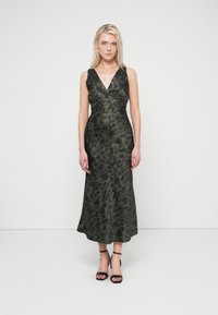 Long, sleeveless dress in dark green with a floral pattern, features a V-neckline and fitted bodice, flaring out to a full skirt. Black strappy heels.