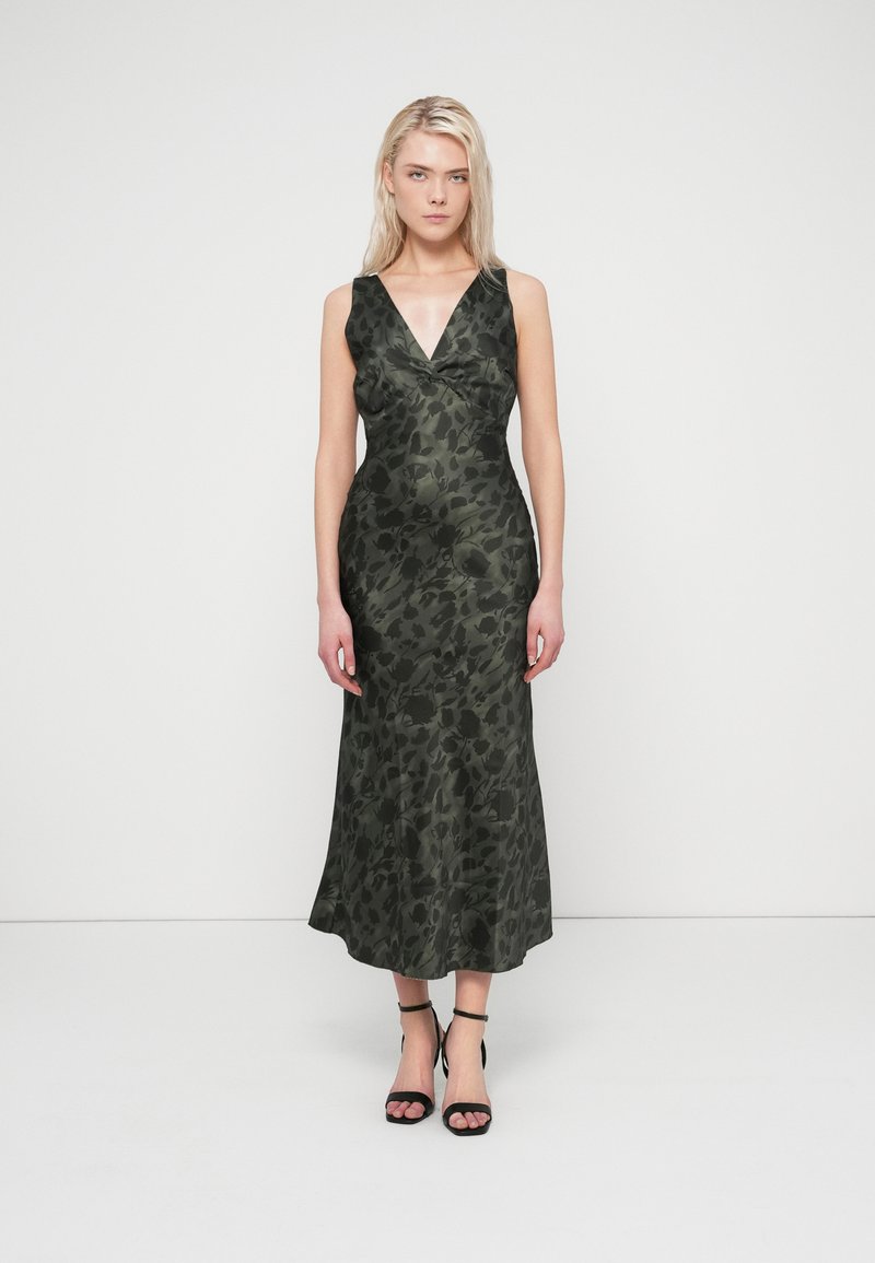 Long, sleeveless dress in dark green with a floral pattern, features a V-neckline and fitted bodice, flaring out to a full skirt. Black strappy heels.