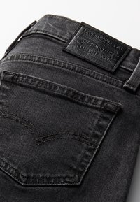 Gros plan de la poche arrière et de la ceinture d’un jean en denim noir avec un patch en cuir noir de la marque Levi Strauss & Co.