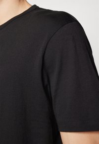 T-shirt nera con design a V. Realizzata in tessuto morbido, presenta maniche corte e una texture liscia con cuciture pulite lungo l'orlo.