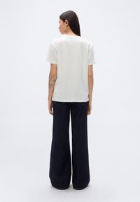 Λευκό βαμβακερό t-shirt με κοντά μανίκια, άνετη γραμμή και στρογγυλή λαιμόκοψη, συνδυασμένο με ευρύχωρα σκούρα μπλε τζιν παντελόνια.