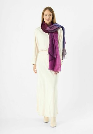 Foulard multicolore dans des teintes de violet drapé sur un blouse couleur crème, associé à une longue jupe crème et des bottines claires.
