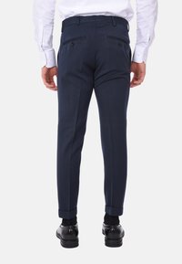 I pantaloni eleganti blu navy presentano una vestibilità slim con doppie tasche posteriori e risvolti. Realizzati in un tessuto morbido, sono abbinati a scarpe nere.