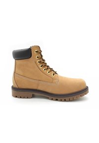 Stivale da lavoro in cuoio tan con lacci, collare imbottito nero e suola robusta, mostrato dal lato esterno su sfondo bianco.