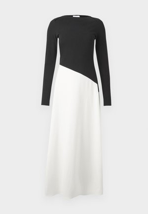 Sukienka z długim rękawem, z czarną górą i białym dołem, z asymetrycznym rozcięciem oraz gładką teksturą materiału.