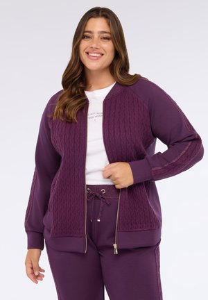 Paarse zip-up jas met een gestructureerde kabelbreisel aan de voorkant en gladde mouwen. Voorzien van een gouden ritssluiting en een koord. Gekocht met bijpassende broek.