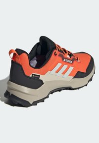 Herrers trailskor i orange och svart, med en andningsbar ovandel, reflexdetaljer, en dämpad sula och en texturerad, slitstark yttersula.