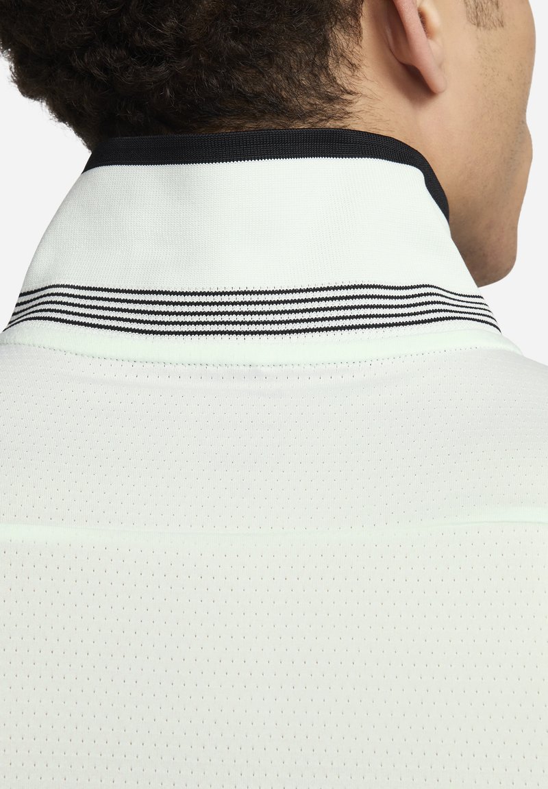 Camisa polo blanca con una tela texturizada y perforada. Presenta un cuello con rayas negras y un diseño de cuello liso y estructurado.