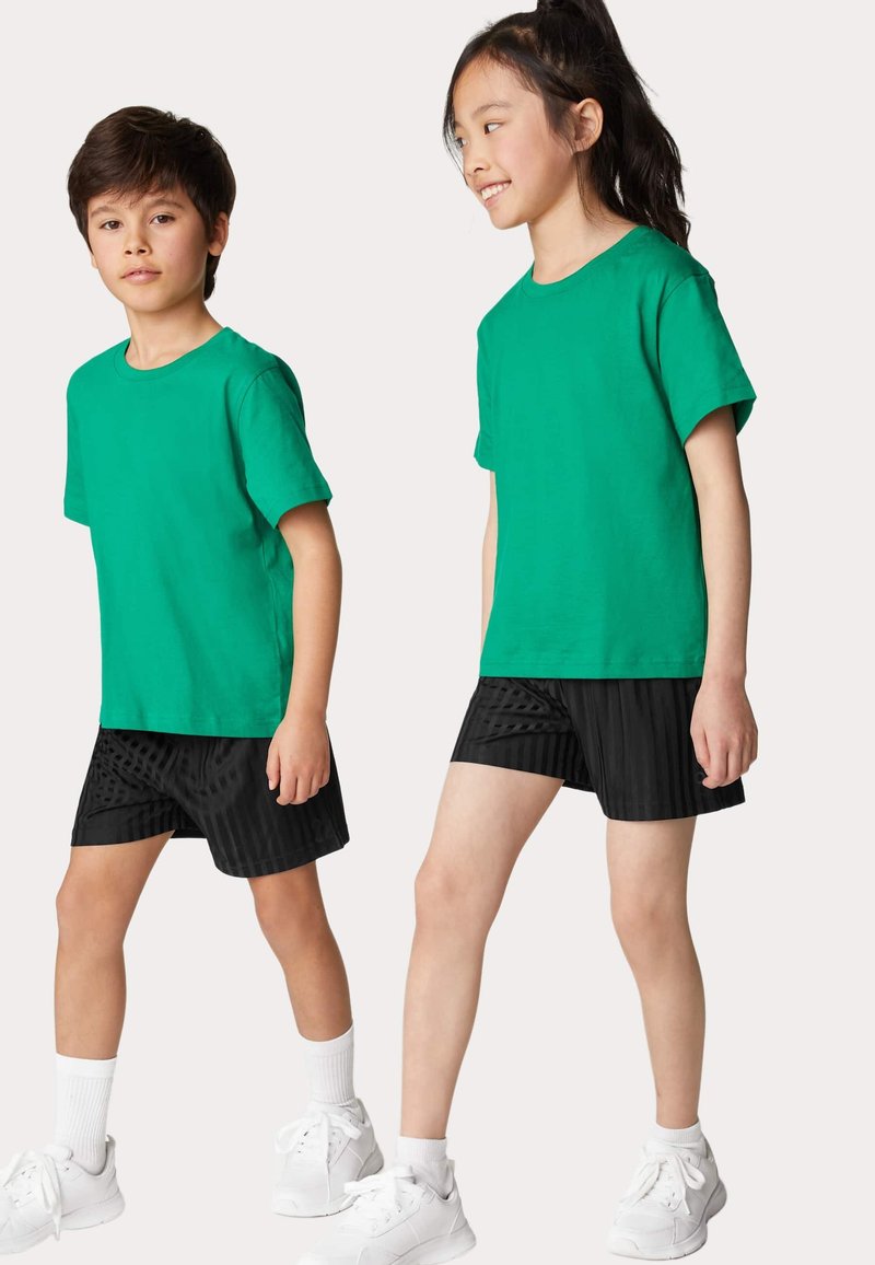Zielone bawełniane t-shirty w połączeniu z czarnymi szortami z teksturowanym wzorem pasków. Obie osoby noszą białe sneakersy i skarpetki.