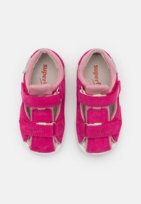 Vaaleanpunaiset mokkanahkaiset lasten sandaalit, joissa on säädettävät tarranauhat, pehmeä sisus ja kumipohjat, joissa on valkoisia yksityiskohtia.