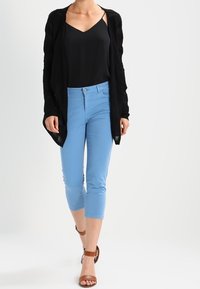 Black open cardigan over a black tank top, paired with light blue cropped pants and brown ankle strap sandals. Smooth fabric, relaxed fit.