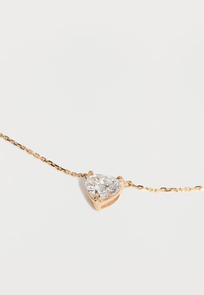 Collier délicat en chaîne d'or avec pendentif en forme de cœur en pierre précieuse claire, serti dans un chaton en or sur fond blanc.
