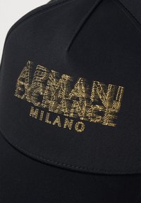 Fekete baseball sapka ívelt karimával, textúrált arany logóval, amelyen az "ARMANI EXCHANGE MILANO" felirat szerepel. Simább anyag, varrott díszítésekkel.