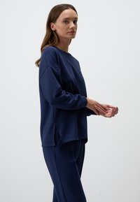 Felpa blu navy con vestibilità comoda, scollo rotondo e aperture laterali. Realizzata in tessuto morbido, abbinata a pantaloni blu navy coordinati.