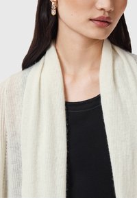 Lättvikts ribbad cardigan i creamfärg med mjuk textur, lagd över en tight svart topp, med öppna kanter och subtila detaljer.
