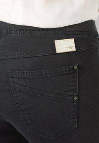 Pantalones de mezclilla negros con un bolsillo trasero cosido, detalle de botón de metal y una pequeña etiqueta texturizada en la cintura.