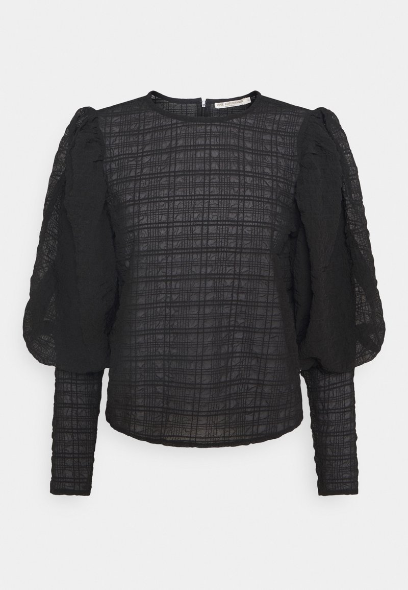 Czarna bluzka z długim rękawem, wykonana z teksturowanej tkaniny, z wzorem w kratę oraz marszczonymi bufiastymi rękawami. Wysoki dekolt i zapięcie z tyłu na środku.