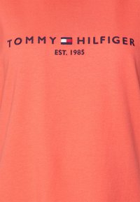 Camiseta de algodón coral con cuello redondo, con el bordado "TOMMY HILFIGER EST. 1985" en azul marino, acentuado por un pequeño diseño de bandera.