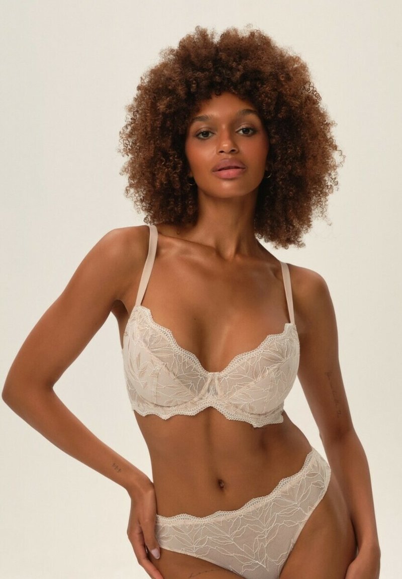 Beżowy zestaw biustonosza i fig z koronką, zdobiony haftem kwiatowym, z regulowanymi ramiączkami, falbaniastymi brzegami oraz miękką teksturą.