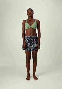 Zelená braletka s tenkými ramienkami, skombinovaná s čiernou sukňou s kvetinovým vzorom v purpurovej a bielej farbe. Mäkká látka, elastický pás.