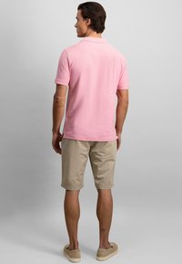 Rosa kortermet polo skjorte med klassisk krage, kombinert med beige shorts. Modellen vender bort, og viser et enkelt design og lett stoff.