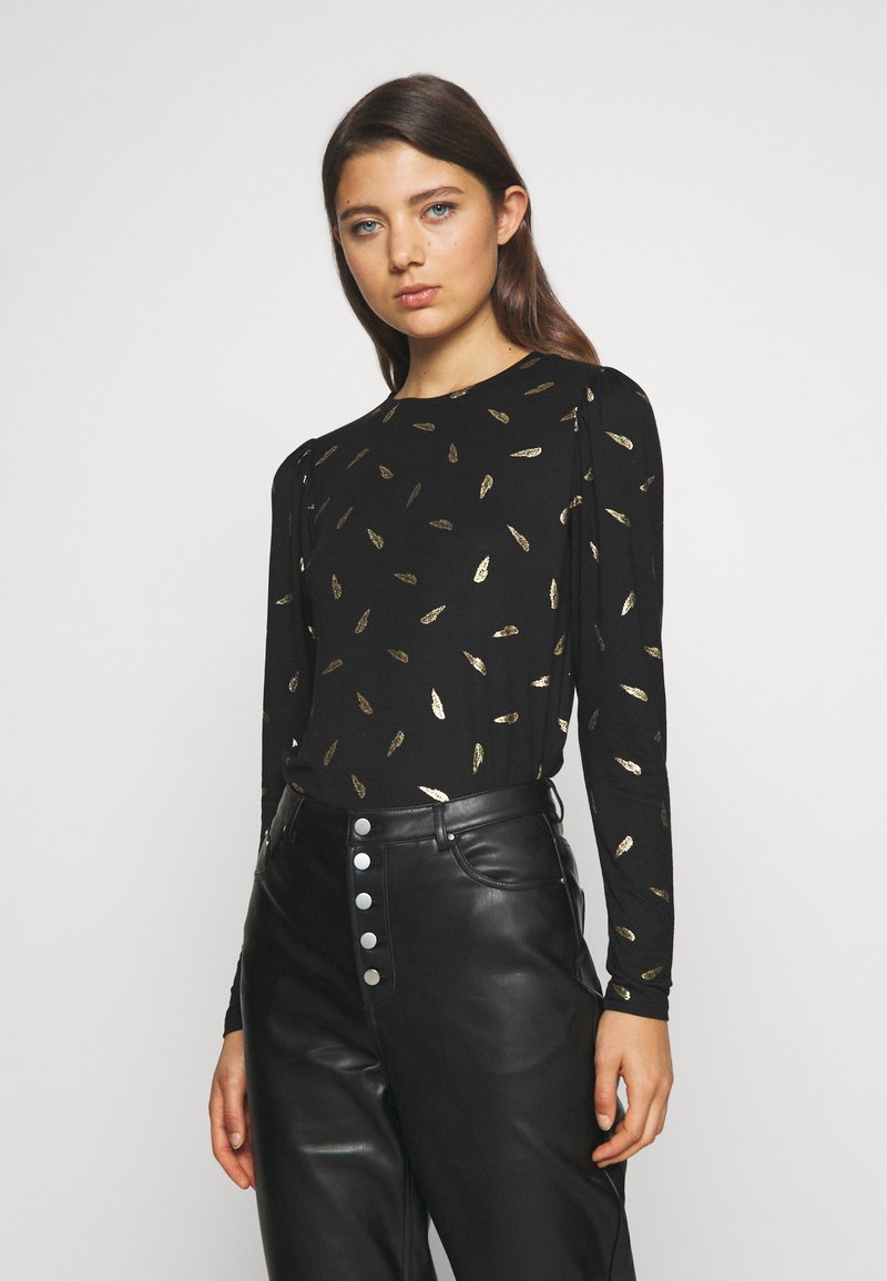 Top preto de mangas longas com um padrão de folhas em dourado. O tecido parece suave, com ligeiro brilho. Combinado com calças de couro pretas de cintura alta.