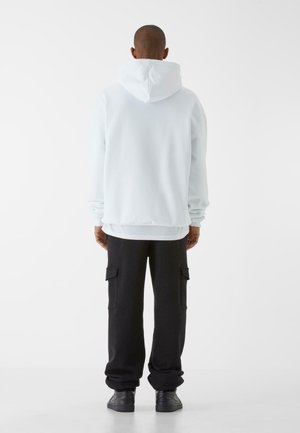 Lyseblå hættetrøje med en afslappet pasform og stor hætte, parret med sorte cargo-bukser med sidelommer og en opsmøgning i kanten. Sorte sneakers.